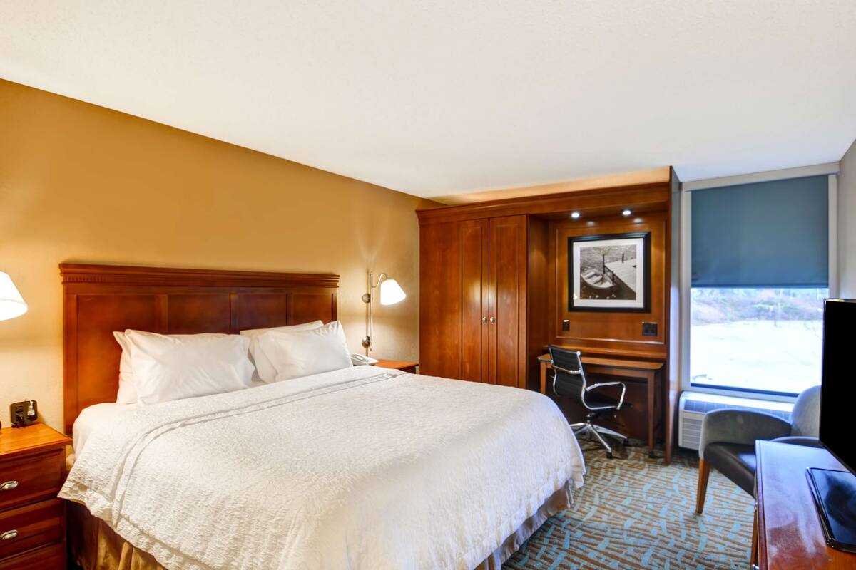 Ein Hotelzimmer mit einem großen Bett, einem Schreibtisch, einem Stuhl und einem Fernseher.