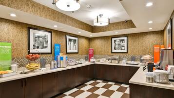 Una cocina de hotel con piso a cuadros, cuadros en la pared y diversos alimentos y bebidas sobre la encimera.