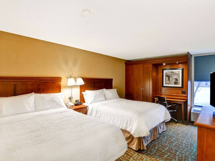 A hotel room with two beds, a desk, a chair, a television, and a framed picture on the wall.