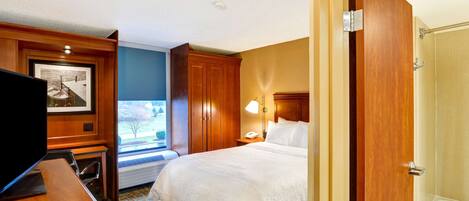 A hotel room with a bed, a desk with a television, a window, a door, and a bathroom with a bathtub.