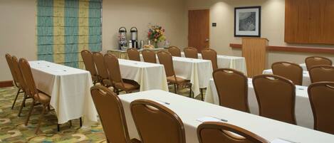 A conference room with multiple tables and chairs, a patterned carpet, a wooden cabinet, and a framed artwork on the wall.