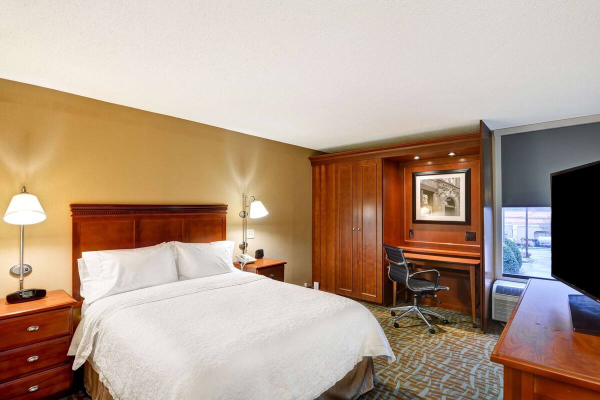Ein Hotelzimmer mit einem großen Bett, einem Schreibtisch, einem Stuhl, einer Schreibtischlampe, einem Telefon und einem Bild an der Wand.