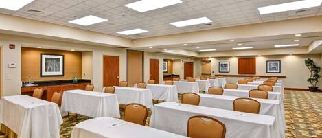 A conference room with multiple tables, chairs, and a kitchenette area.