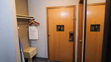 A hallway with two wooden doors, a small white cabinet, and a coat rack with hangers.