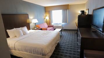 A hotel room with a large bed, a desk with a TV, a chair, and a window with curtains.