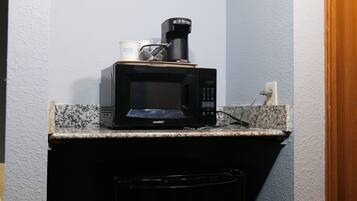 A kitchen with a microwave on the countertop, a coffee maker, and a cup.