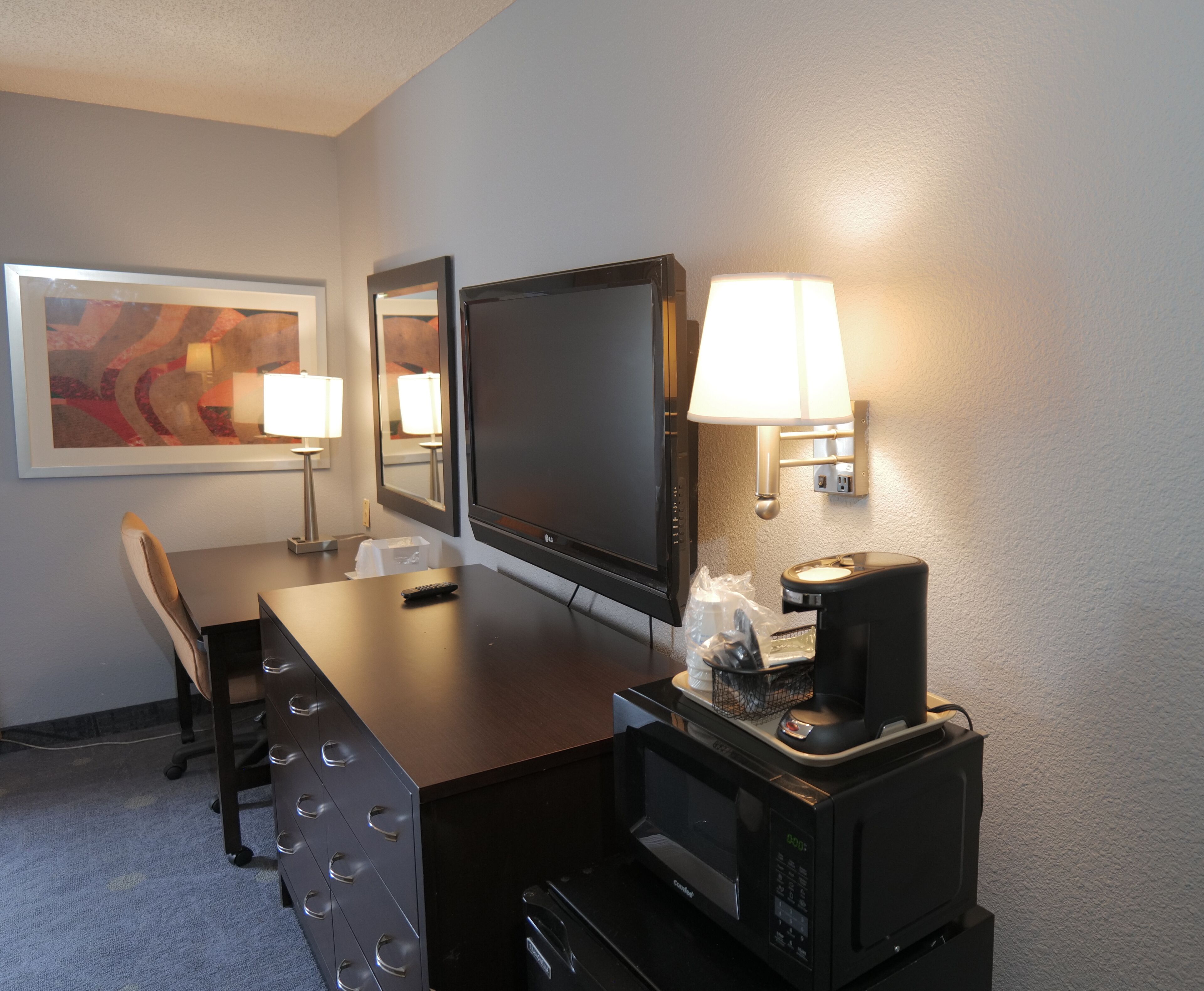 Une chambre d’hôtel équipée d’un bureau, de chaises, d’un téléviseur à écran plat, d’une machine à café et d’un four à micro-ondes.