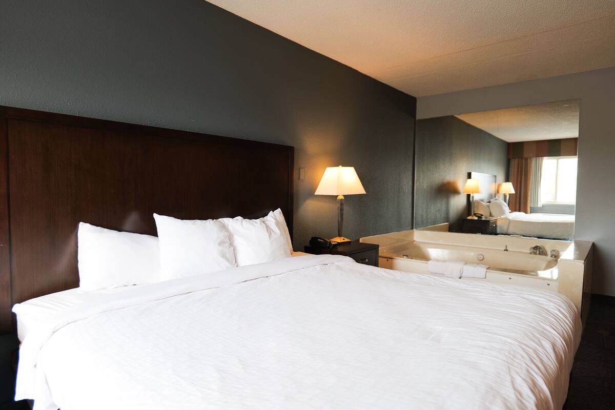 A hotel room with a large bed, a nightstand with a lamp, a bathroom with a sink and mirror.