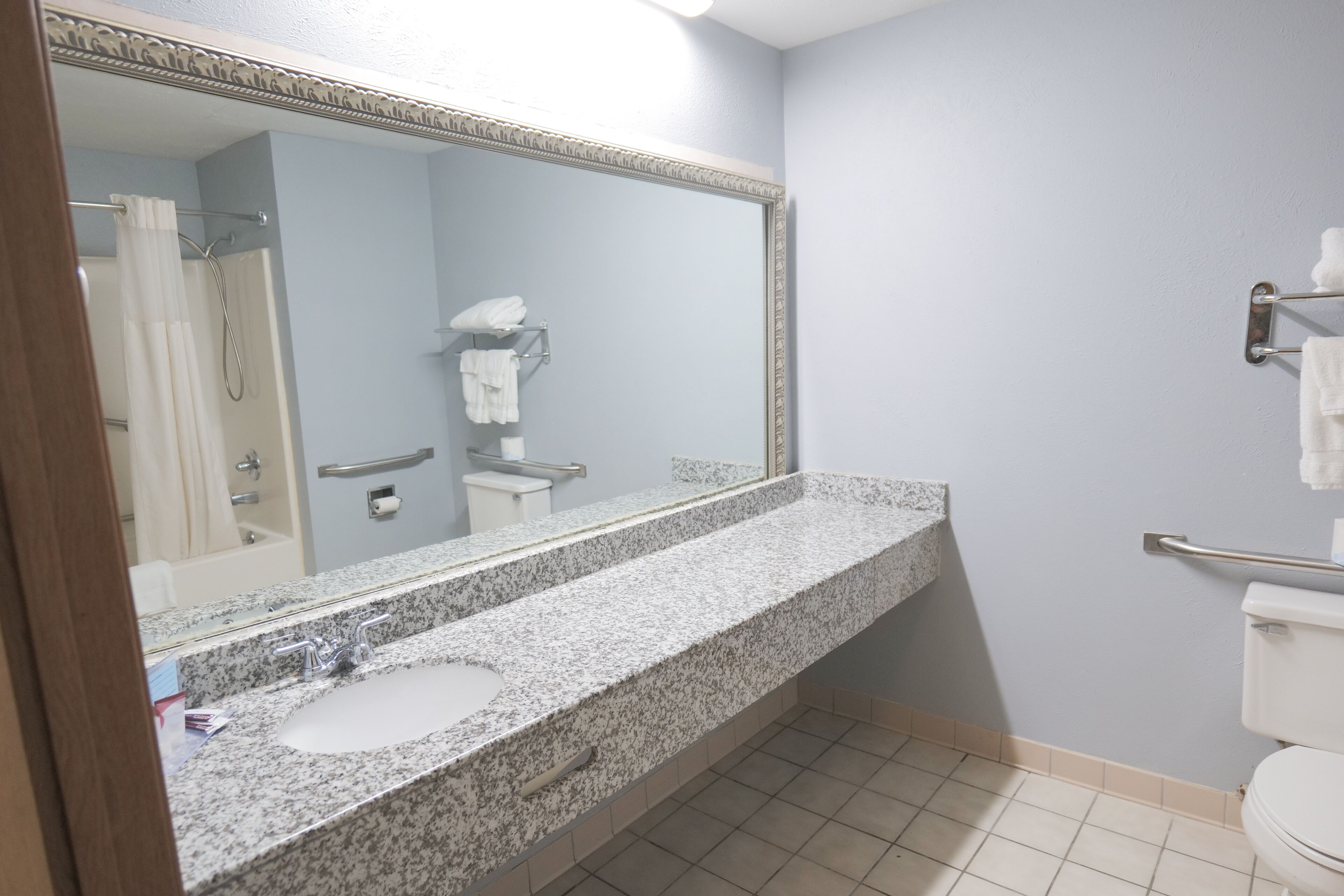 A bathroom with a granite countertop sink, a large mirror, a towel rack, and a shower curtain.