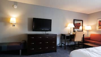 Een hotelkamer met een flatscreen televisie aan de muur, een donker houten dressoir, een rode bank, een klein bureau met stoel en twee wandlampen.