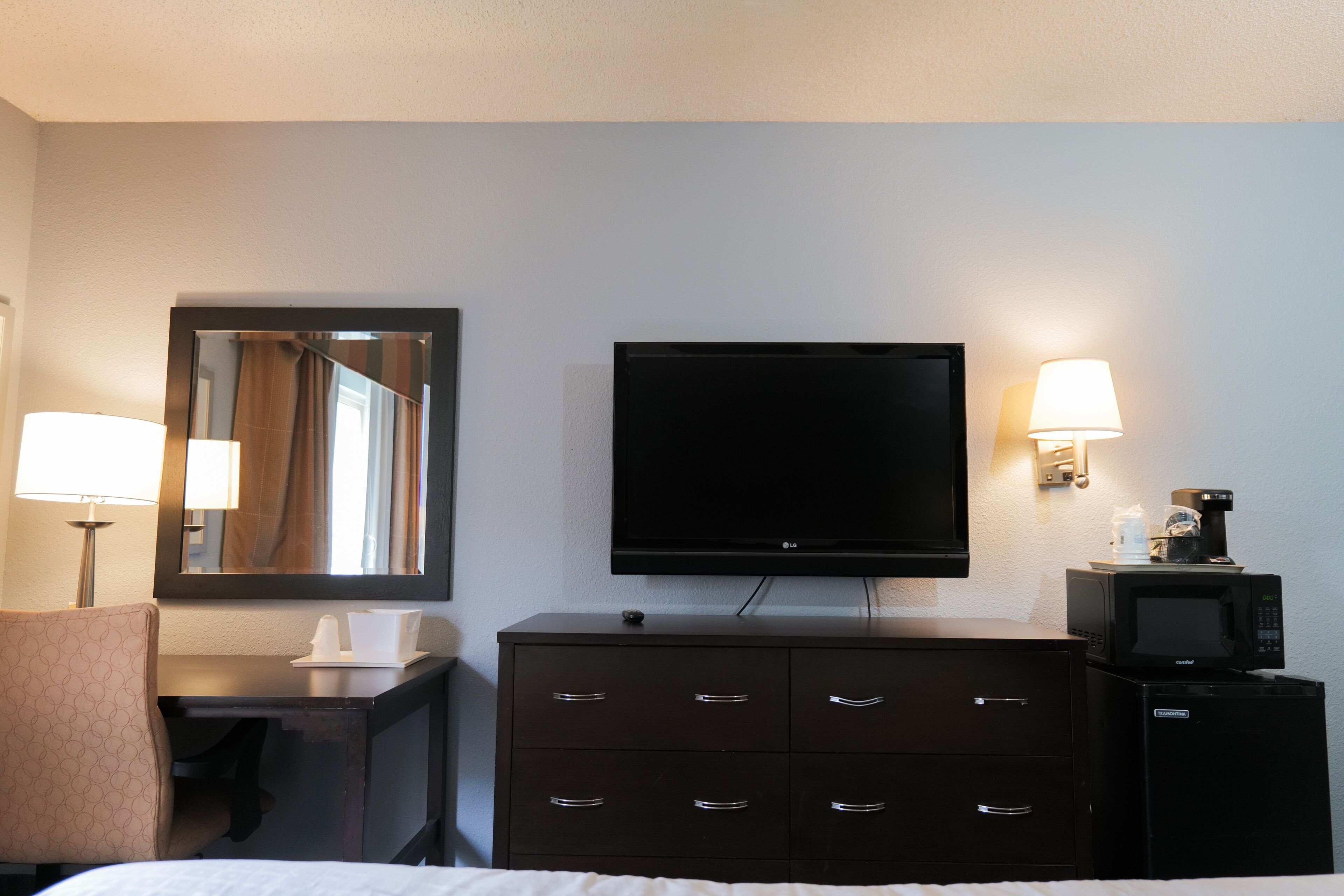 A hotel room with a bed, a desk with a lamp, a dresser, a television, and a microwave.