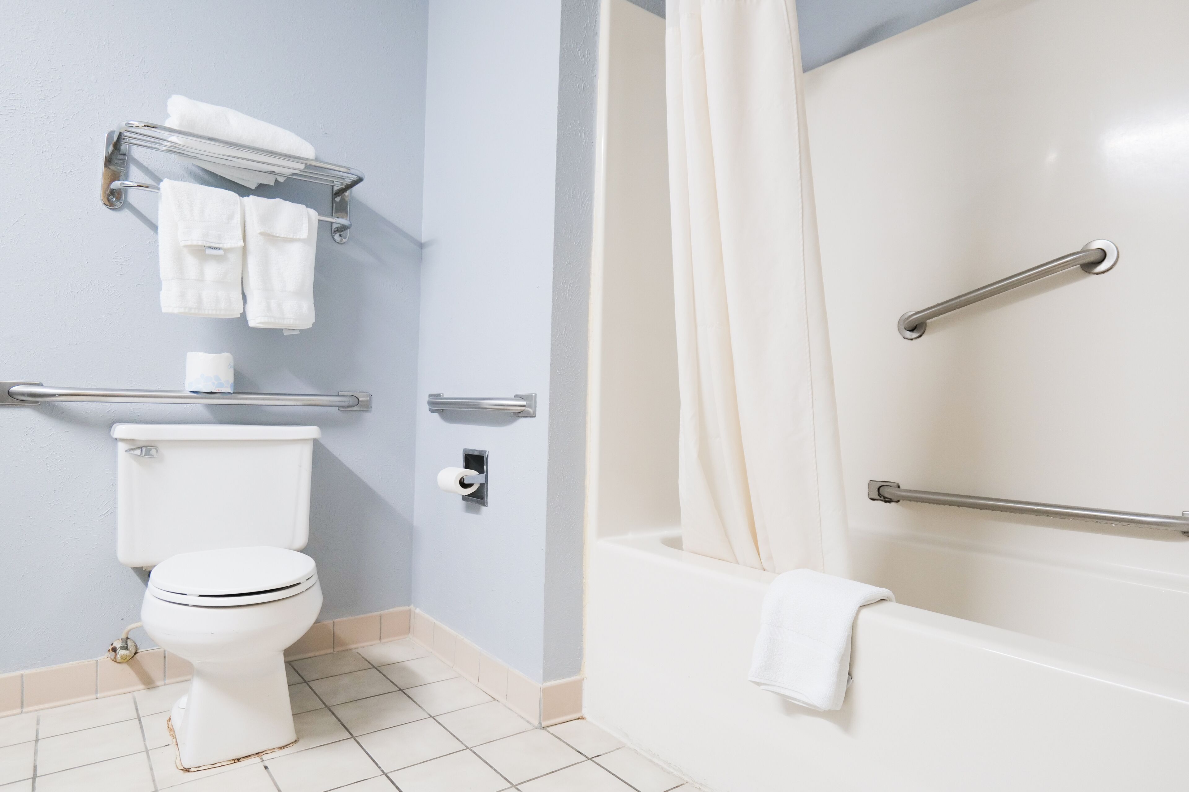 Et badeværelse med toilet, håndklæderække, bruser med gelænder og badekar.