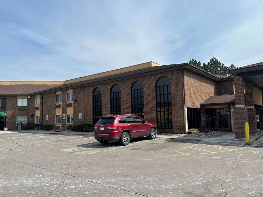 A red SUV parked in a parking lot in front of a brick building with multiple windows and a covered entrance.