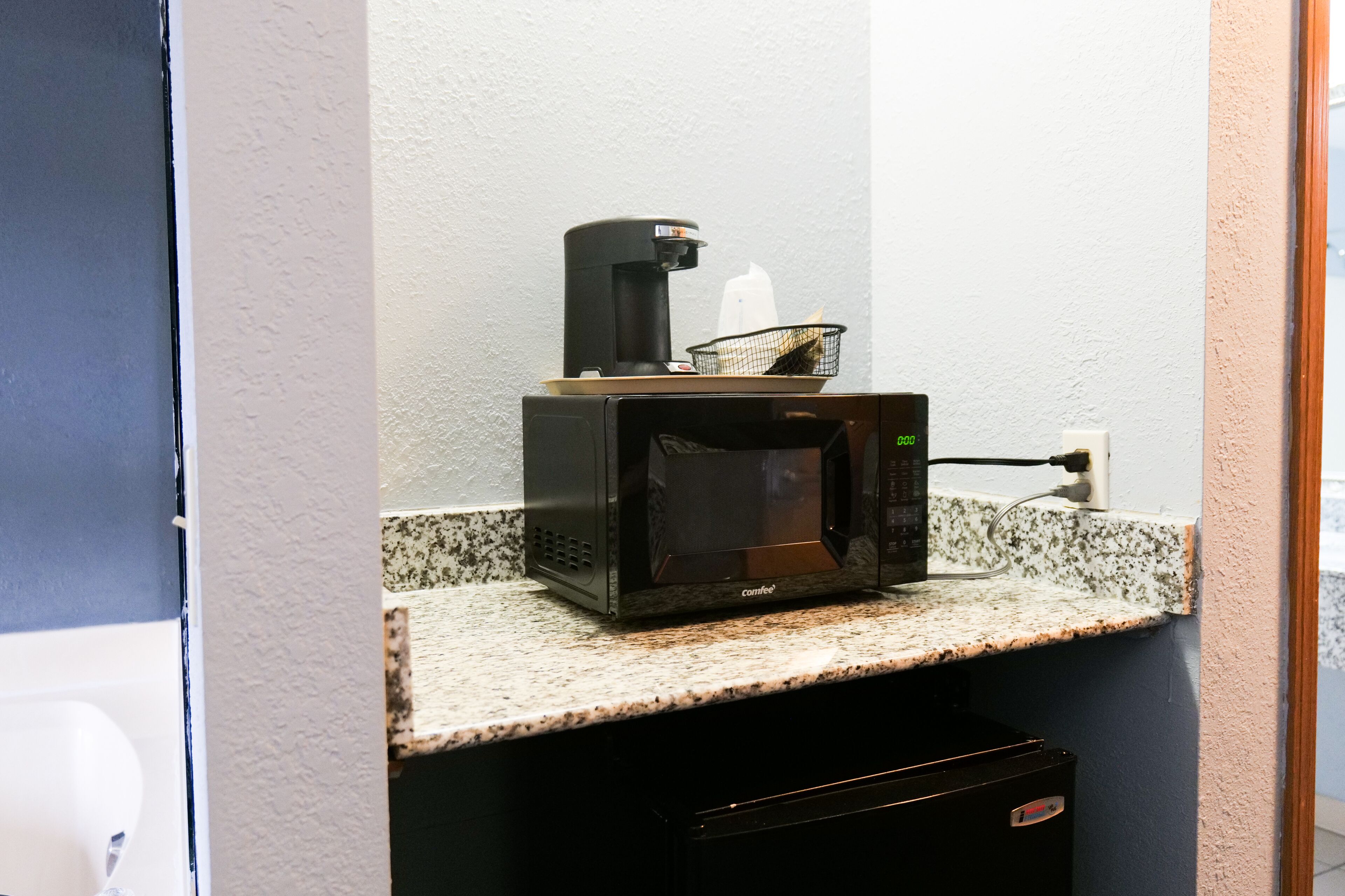 A microwave on a granite countertop with a coffee maker and a basket.