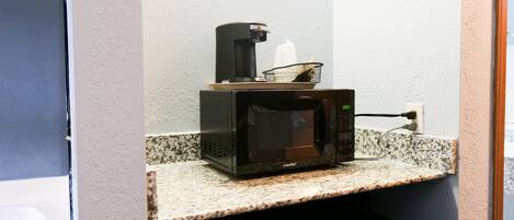 A microwave on a granite countertop with a coffee maker and a basket.