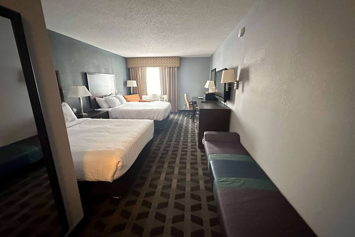 A hotel room with two beds, a desk with a television, and a seating area.