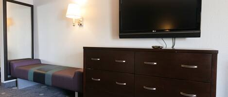 A hotel room with a bed, a dresser, a television, and a wall-mounted lamp.