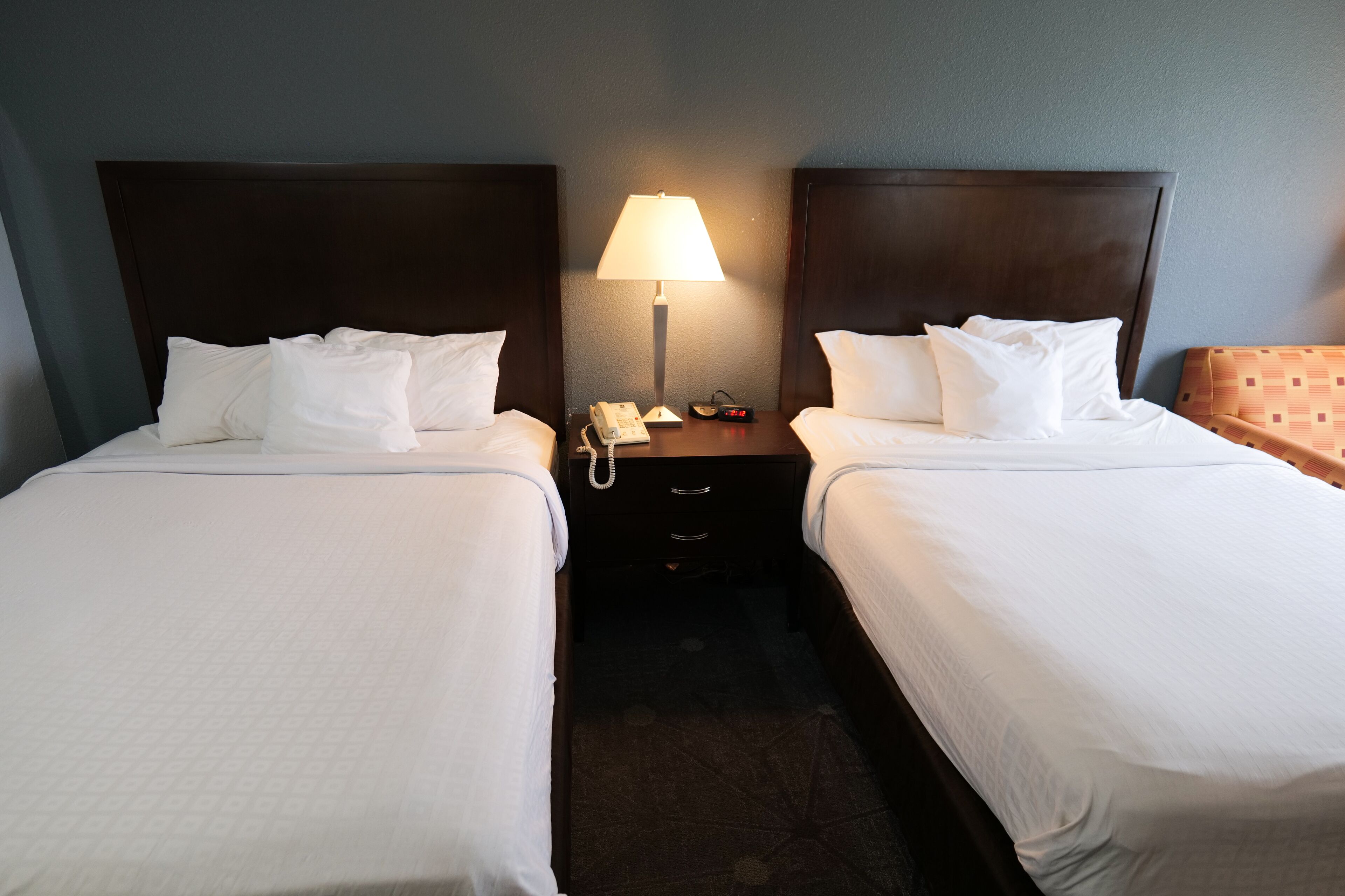 Une chambre d’hôtel avec deux lits simples, une table de chevet avec une lampe, un téléphone et une horloge.