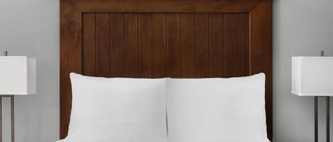 A neatly made bed with a wooden headboard, white bedding, and two bedside lamps on either side.