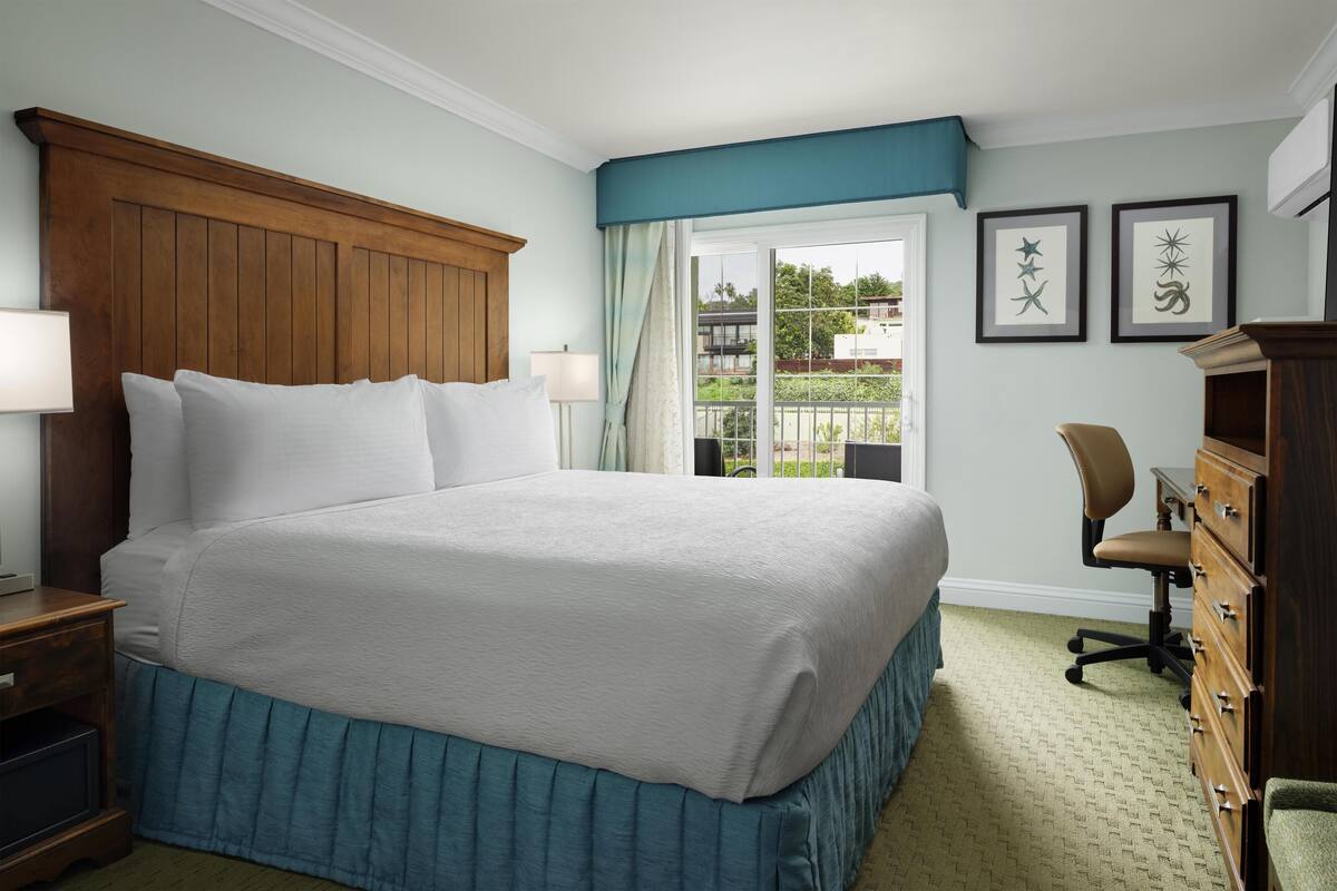 A neatly made bed with a wooden headboard, a desk with a chair, and a dresser.