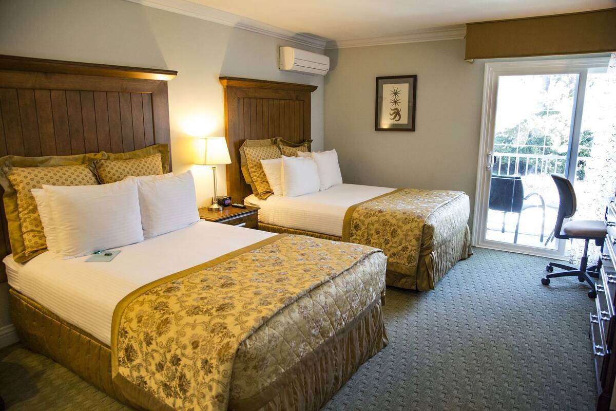 A hotel room with two beds, a desk, a chair, and a balcony with a view.