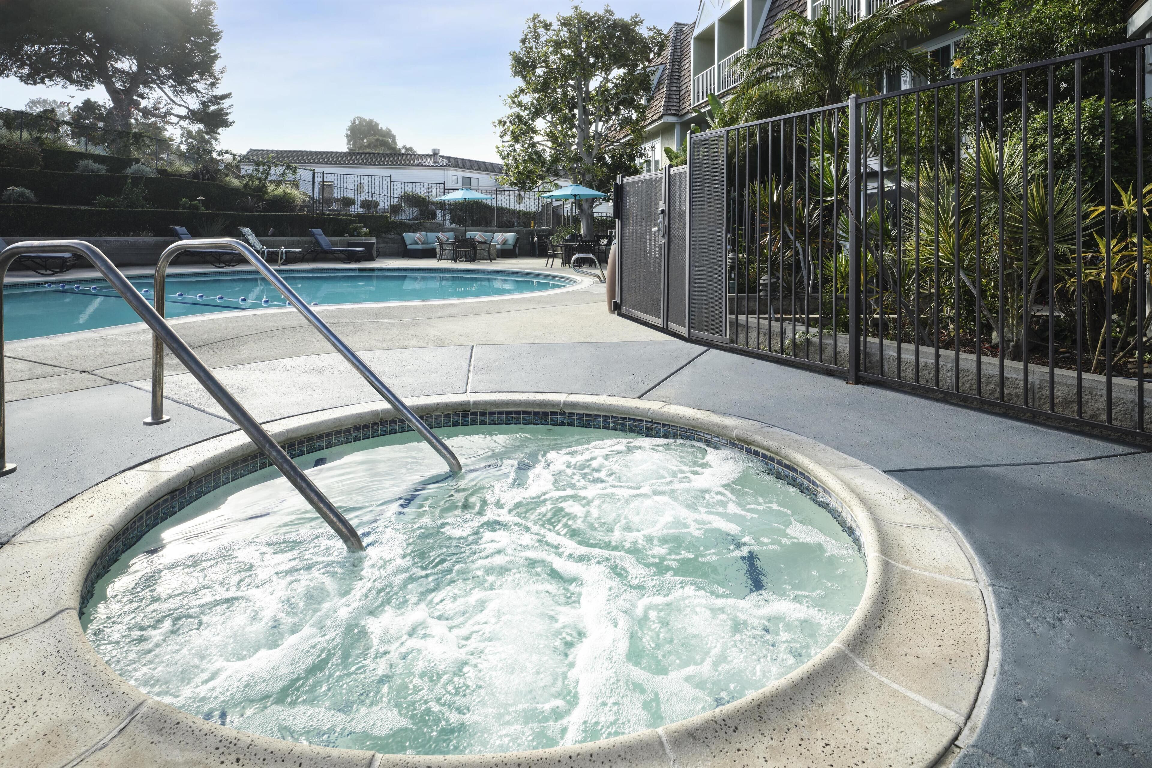 A hot tub with a metal ladder, surrounded by a concrete deck and a metal fence.