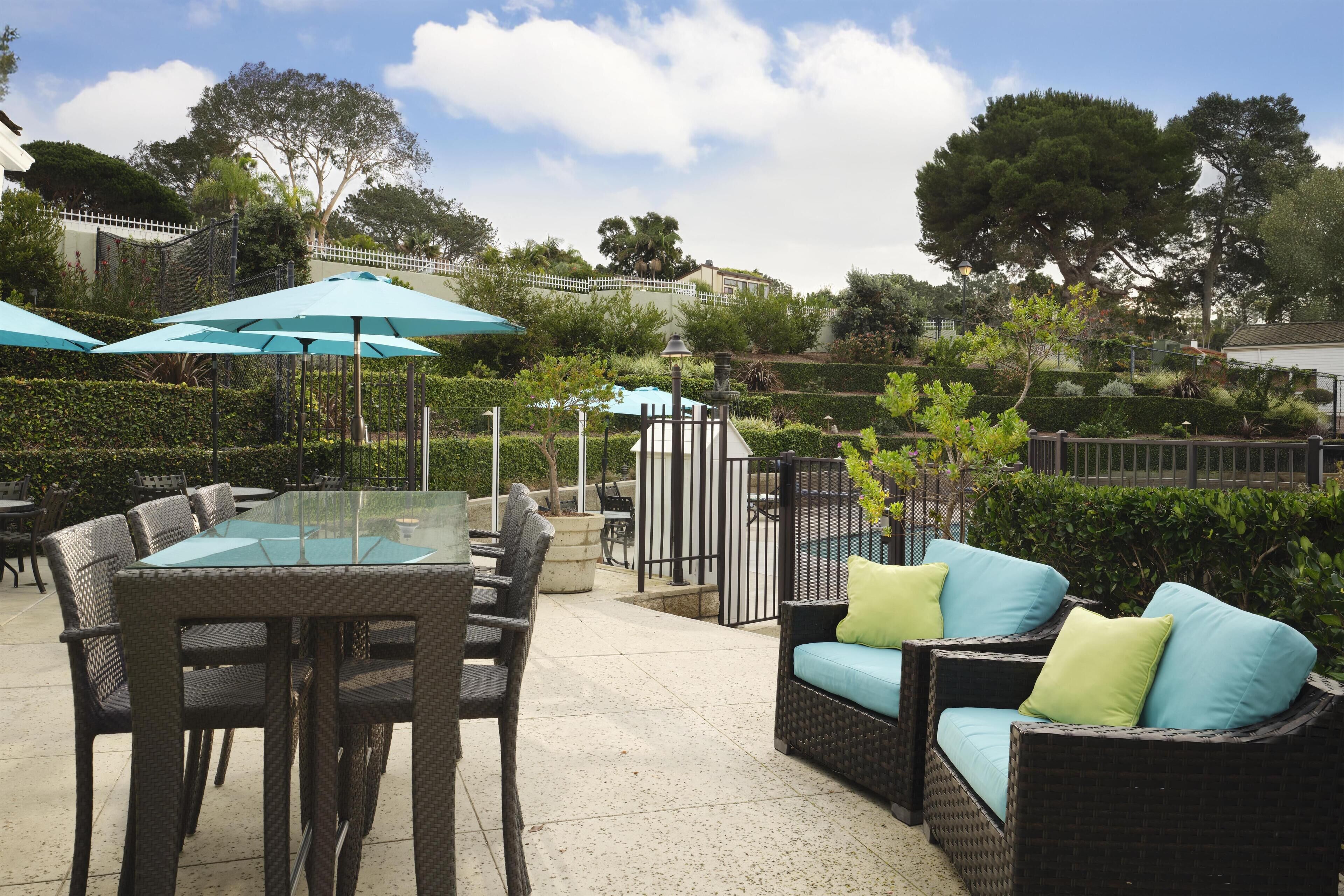 Een terras buiten met rieten meubels, glazen tafels en blauwe parasols.