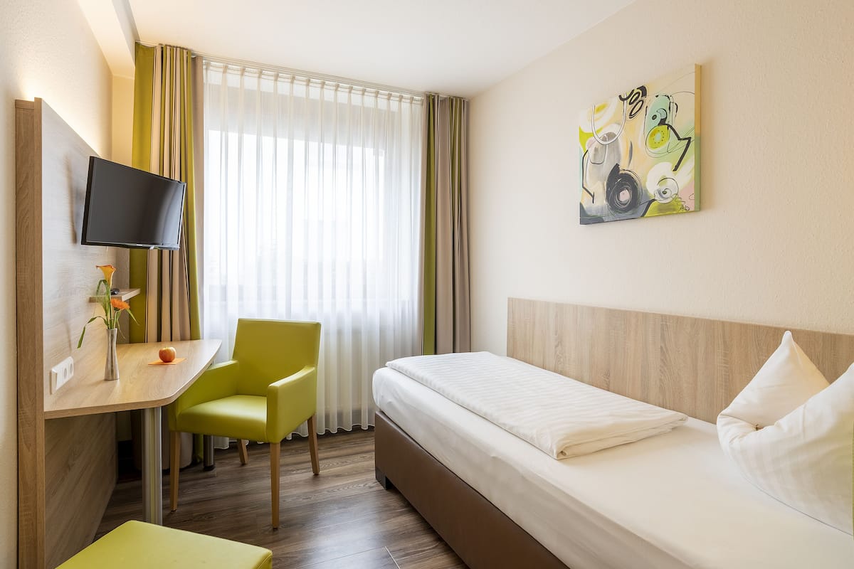 A hotel room with a bed, a desk, a chair, a TV, and a painting on the wall.