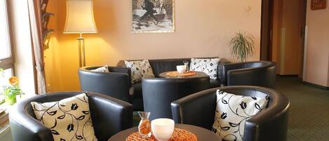 A hotel lobby with leather armchairs, a round table with a candle and a vase, a lamp, and a framed picture on the wall.