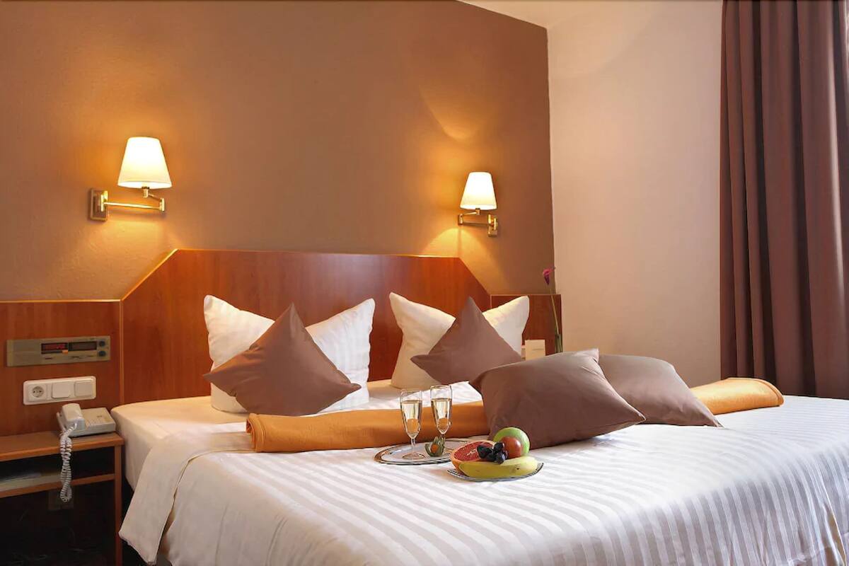 A hotel room with a bed, two bedside lamps, a bedside table with a phone, and a fruit plate on the bed.