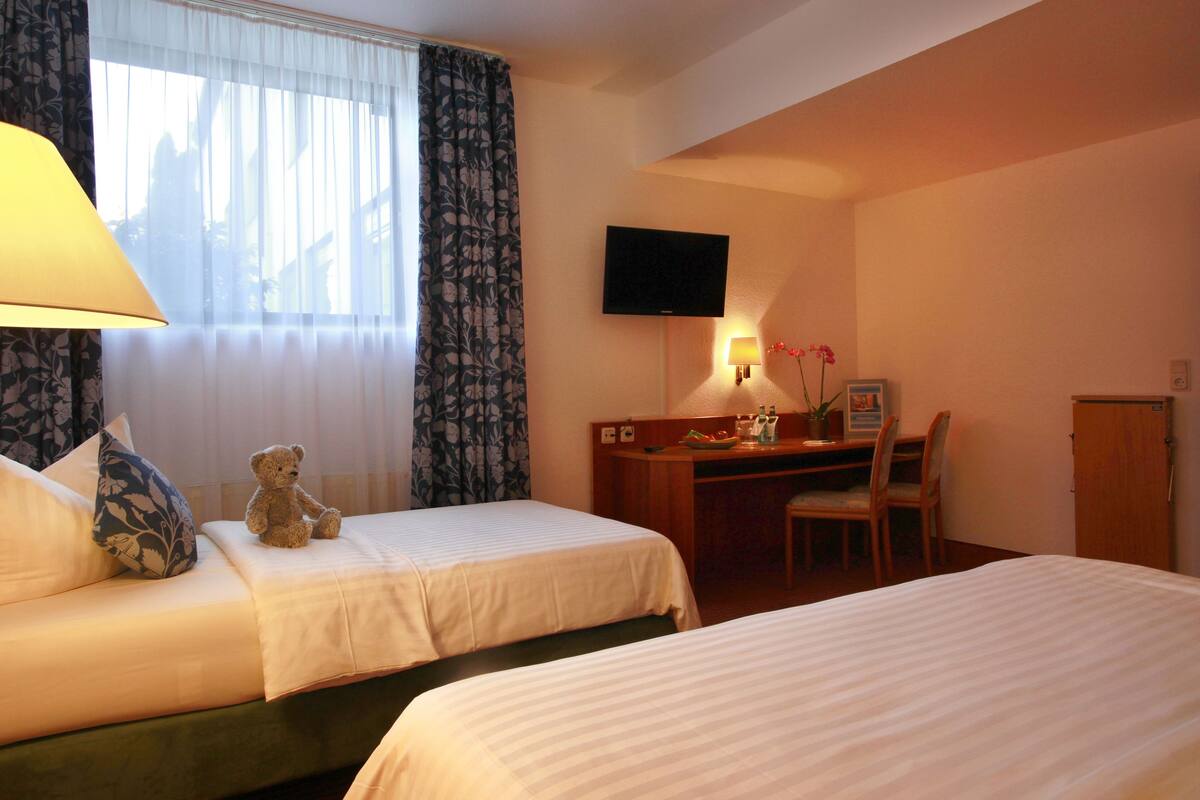 A hotel room with two beds, a desk, a chair, a television, and a window with curtains.