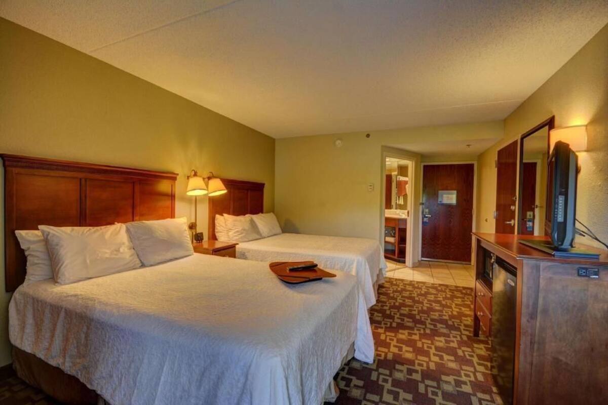 A hotel room with two beds, a desk, a mirror, and a television.