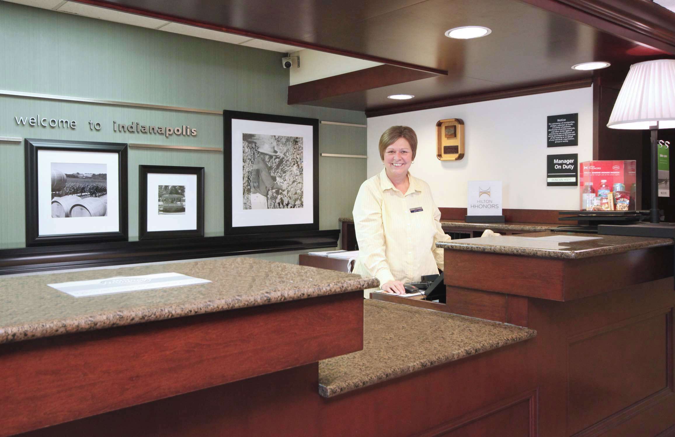 A reception desk with framed historical photos, a welcome sign, and a manager's nameplate.
