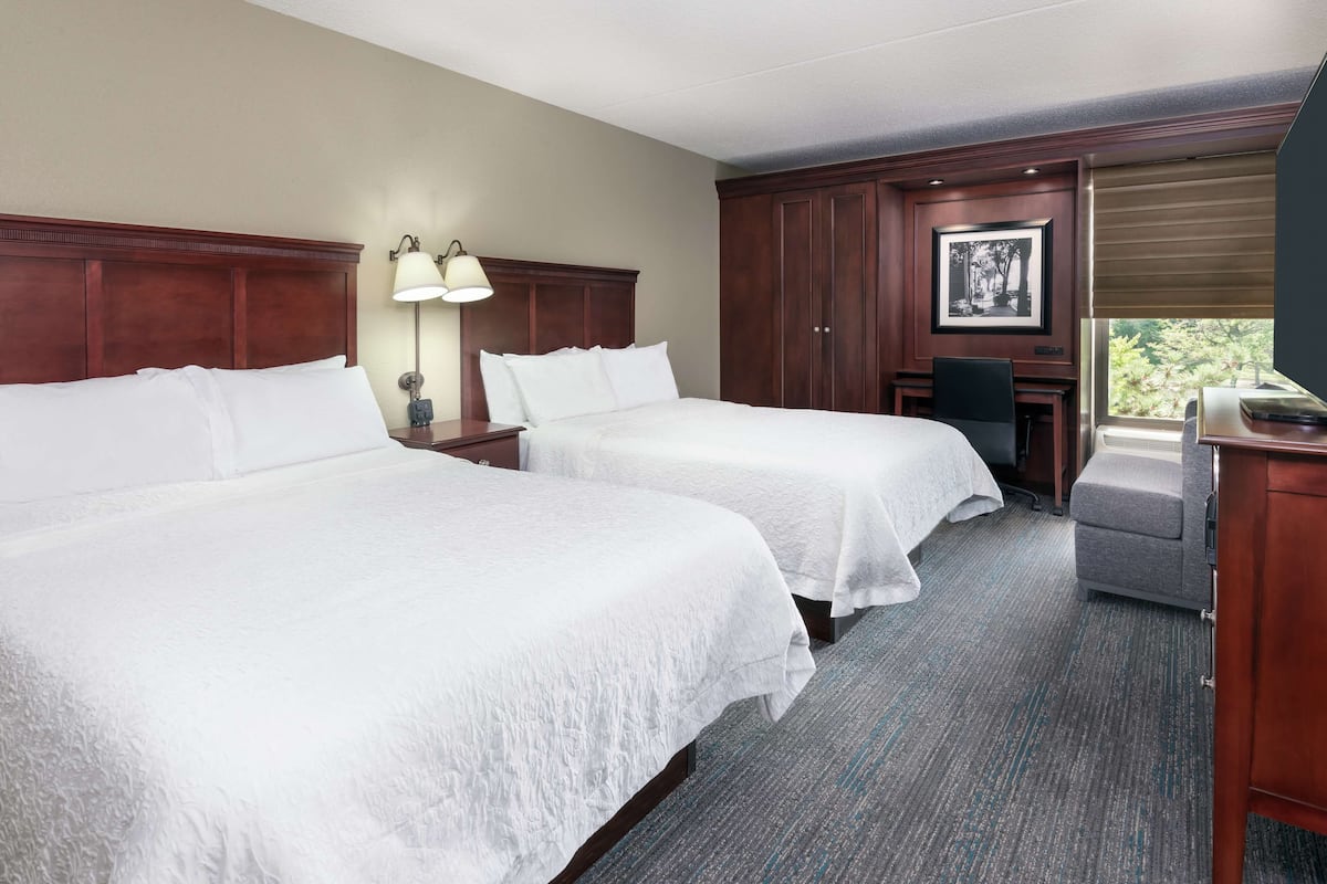 A hotel room with two beds, a desk, a chair, and a window with a view.