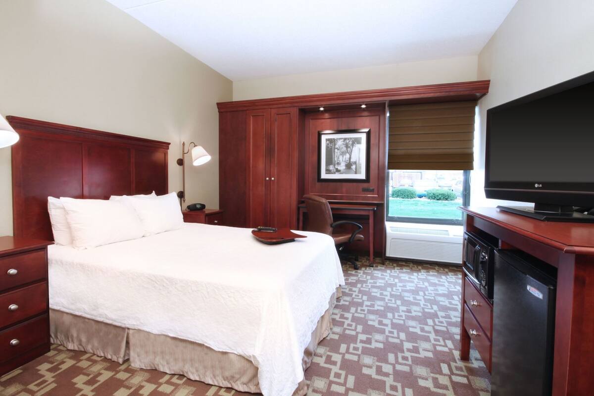 A hotel room with a bed, desk, chair, television, and a window with a view.