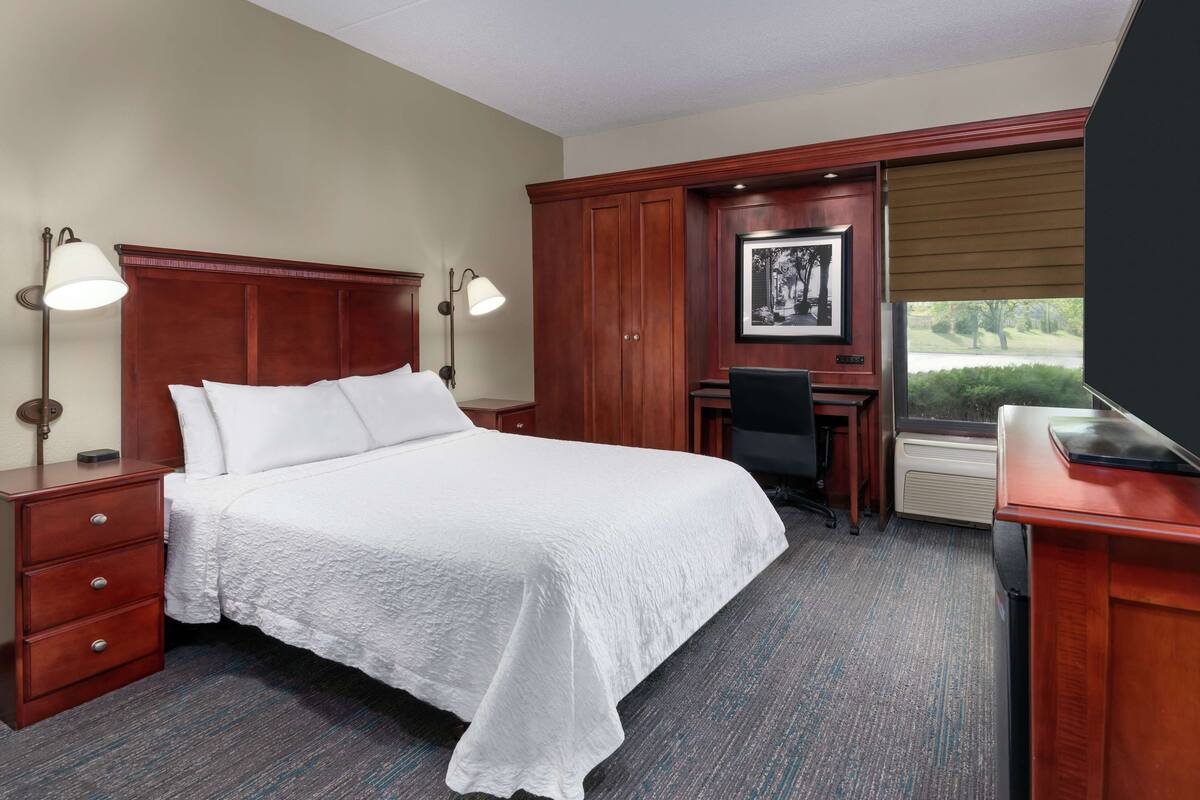 A hotel room with a large bed, a desk, a chair, a lamp, and a picture on the wall.