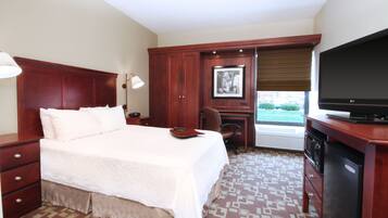 A hotel room with a large bed, a desk with a chair, a television, and a wardrobe.