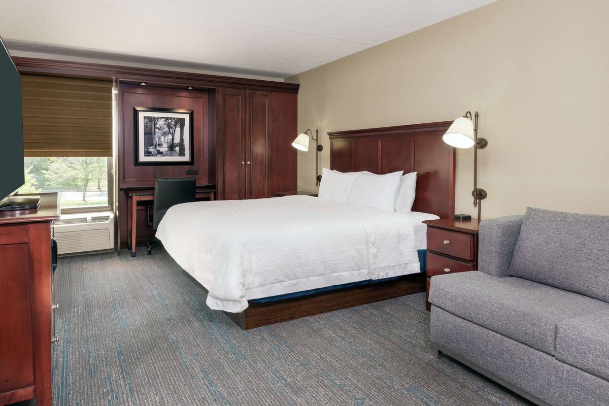 A hotel room with a large bed, a desk, a chair, a sofa, and a picture on the wall.