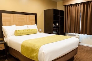 A neatly made bed with white and yellow bedding, a wooden headboard, a brown wardrobe, and a window with curtains. - GlenRock Inn & Suites (Los Angeles)