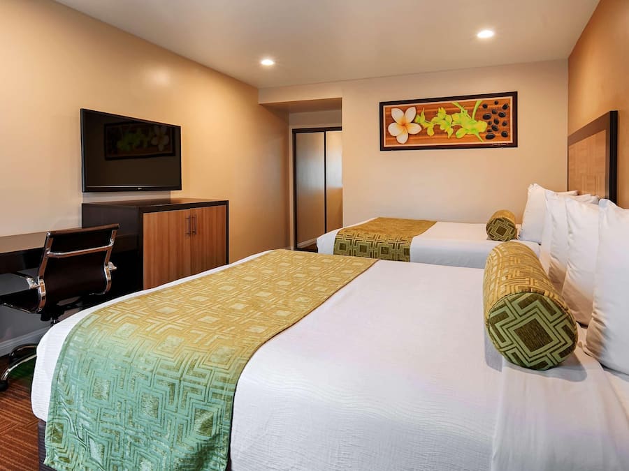 Habitación de hotel con dos camas, un escritorio, una silla y un televisor.