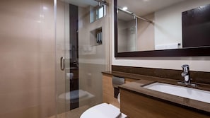 A modern bathroom with a glass shower enclosure, a large mirror, and a wooden vanity with a sink. - GlenRock Inn & Suites (Los Angeles)
