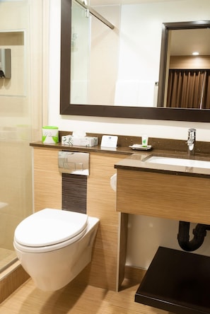 A modern bathroom with a toilet, sink, and mirror. - GlenRock Inn & Suites (Los Angeles)