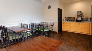 A dining area with a wooden table and chairs, a kitchen with a microwave and juice dispenser, and a clock on the wall. - Best Western Plus Glendale (Los Angeles)