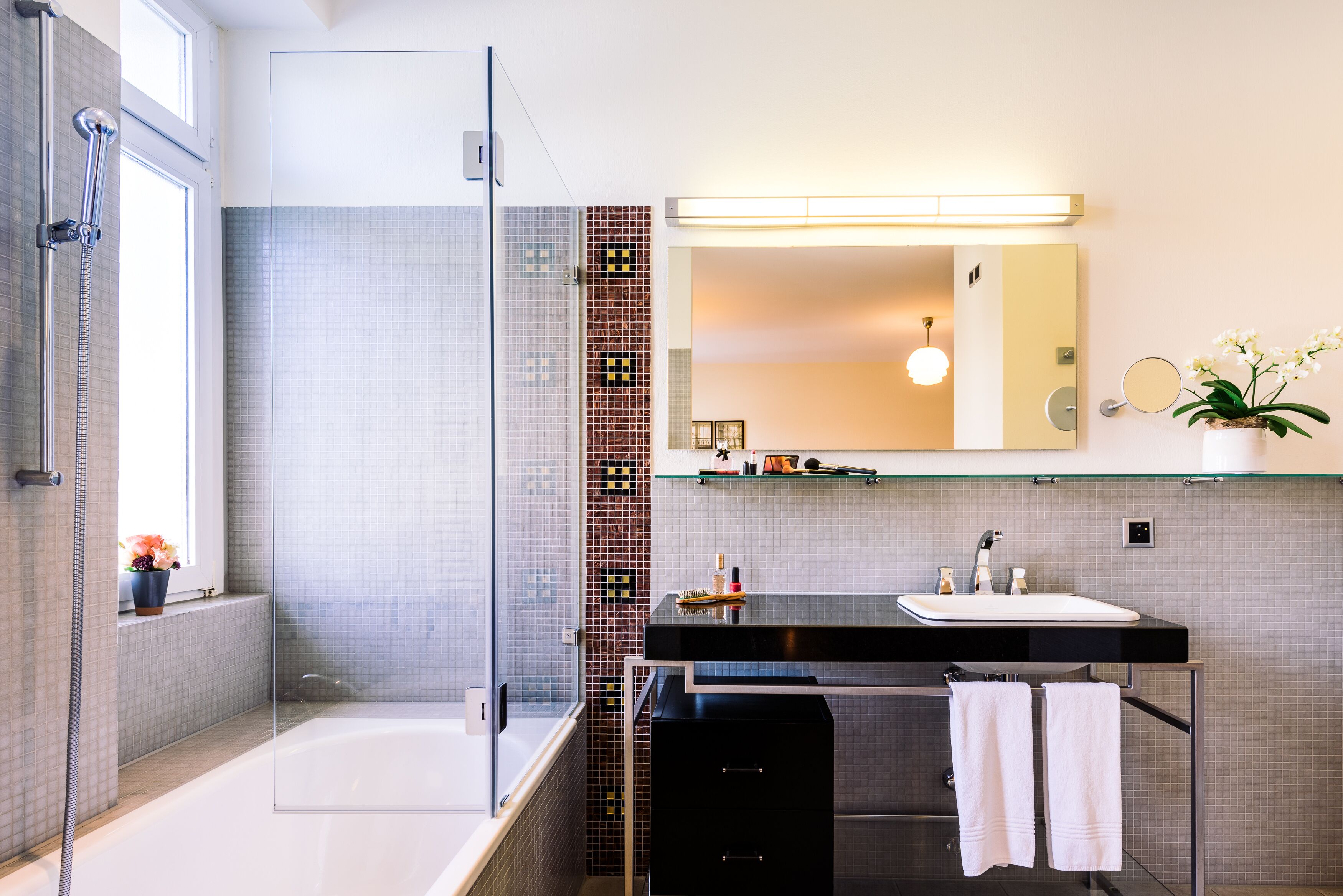 Une salle de bain moderne avec une douche en verre, une baignoire, un meuble-lavabo avec un miroir et une orchidée en pot.
