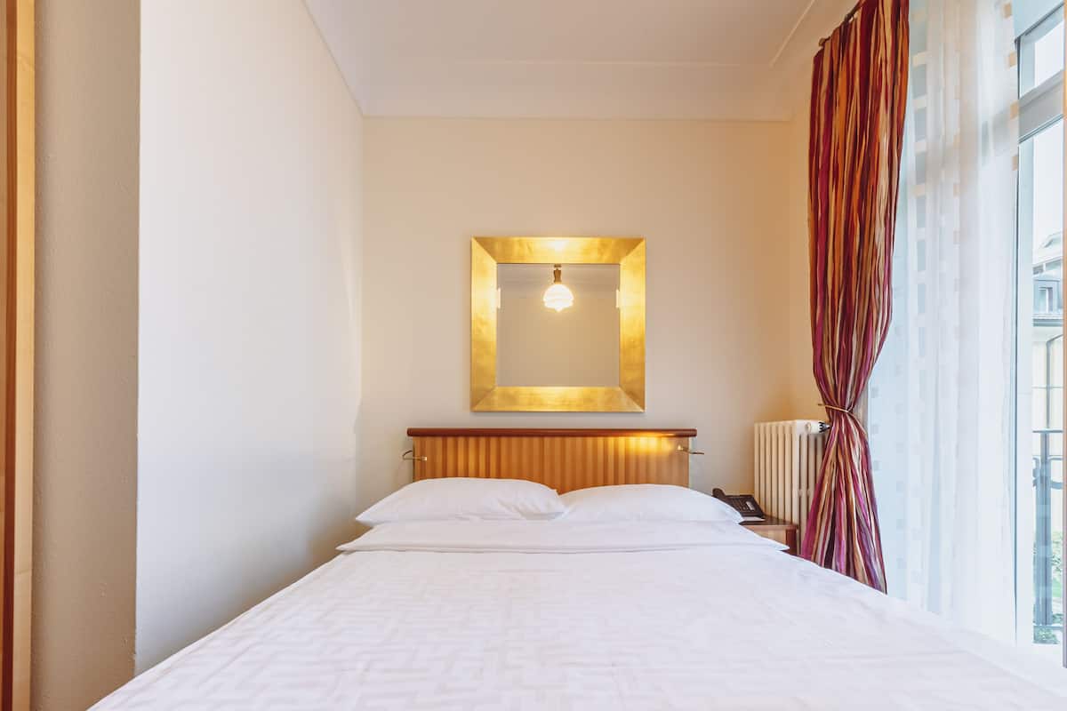 Een hotelkamer met een bed, nachtkastje, spiegel en raam met gordijnen.