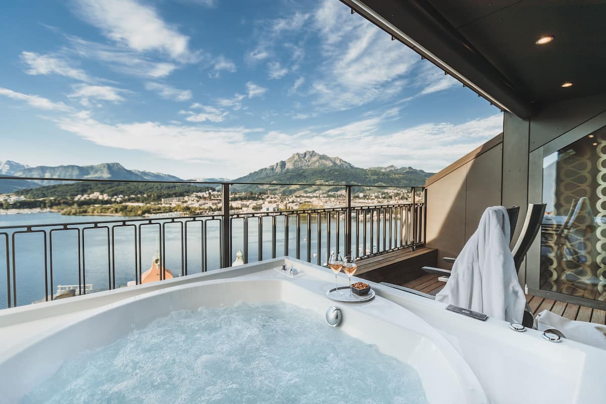 Een balkon met een jacuzzi, uitzicht op een meer en bergen op de achtergrond.