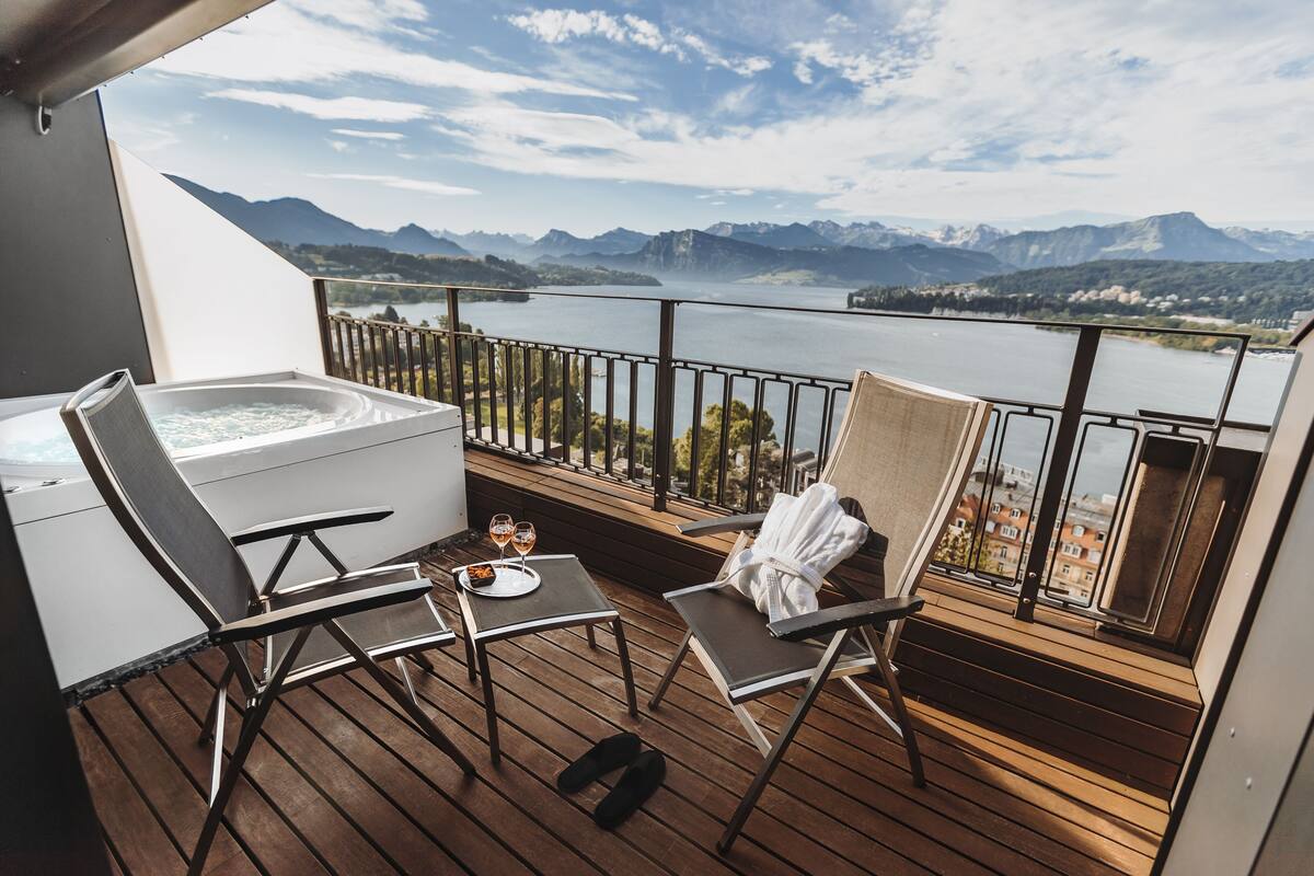 Een balkon met een jacuzzi, twee loungestoelen en een tafel met glazen en een bord.