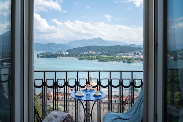 A balcony with a table and chairs, overlooking a lake and a mountainous landscape. - Art Deco Hotel Montana (Lucerne)