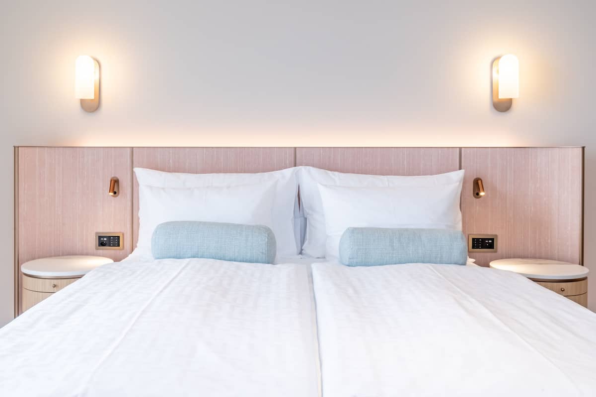 Een tweepersoonsbed met twee nachtkastjes, elk voorzien van een bedieningspaneel, in een moderne hotelkamer.