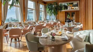 Un restaurante con varias mesas y sillas, ventanas amplias y plantas de interior.